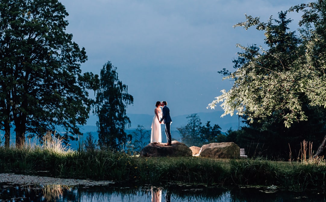 Jung und Wild design: Hochzeitsfotografie im Bayerischen Wald bei Bodenmais: Brautpaar am Weiher in der blauen Stunde mit Gegenlicht