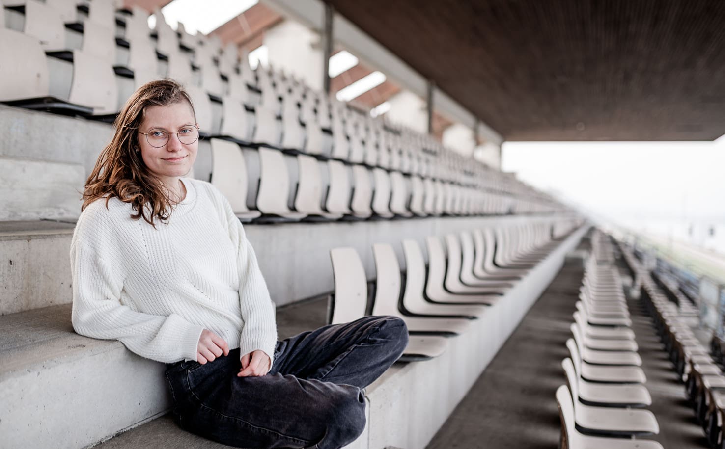 Eine Person sitzt auf einer Tribüne in einem leeren Stadion.