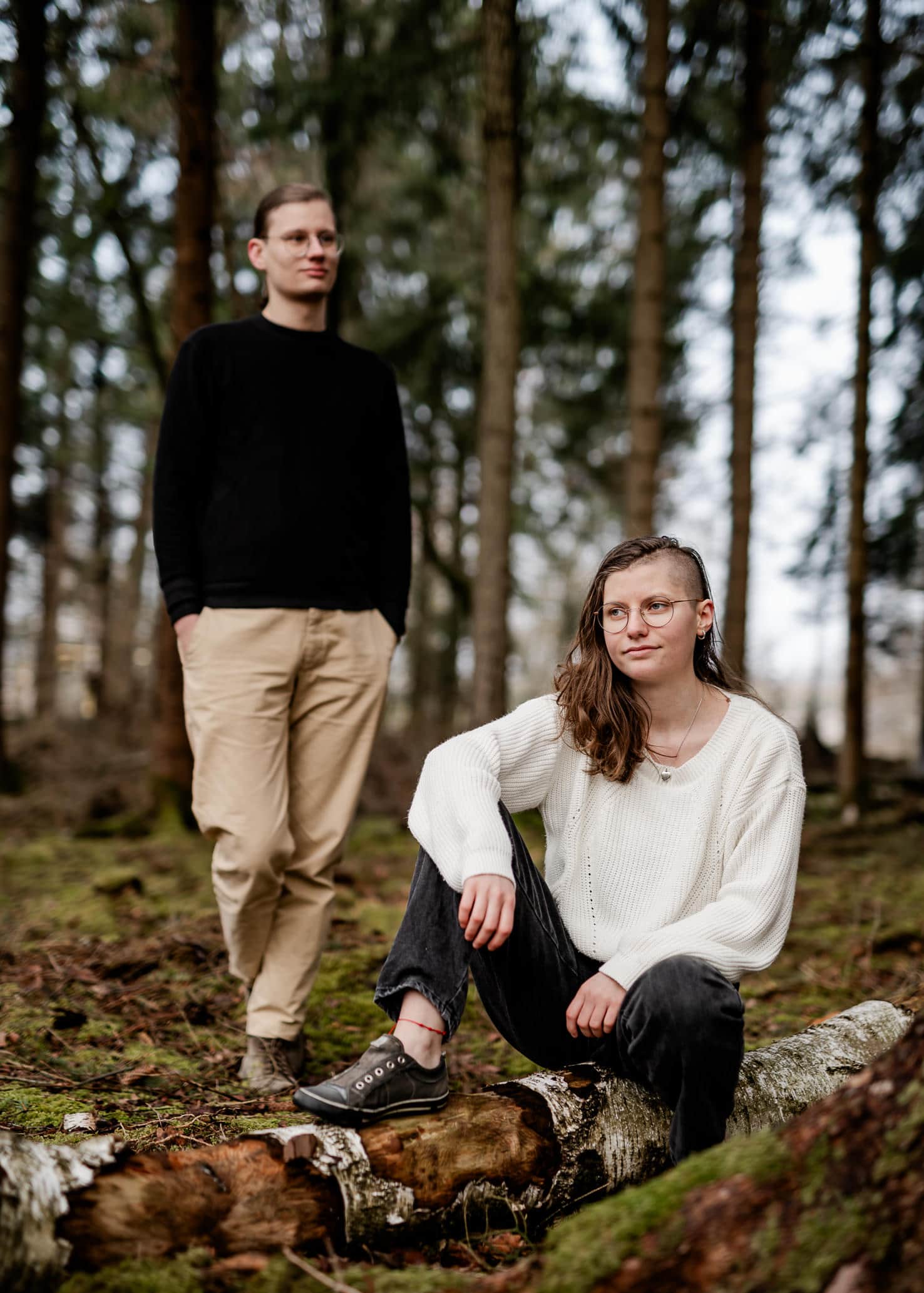 Das Bild zeigt zwei Personen, eine sitzend und eine stehend, in einem Wald.