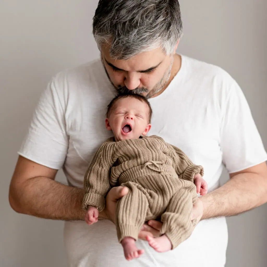 Ein Mann hält liebevoll ein gähnendes Baby im Arm.