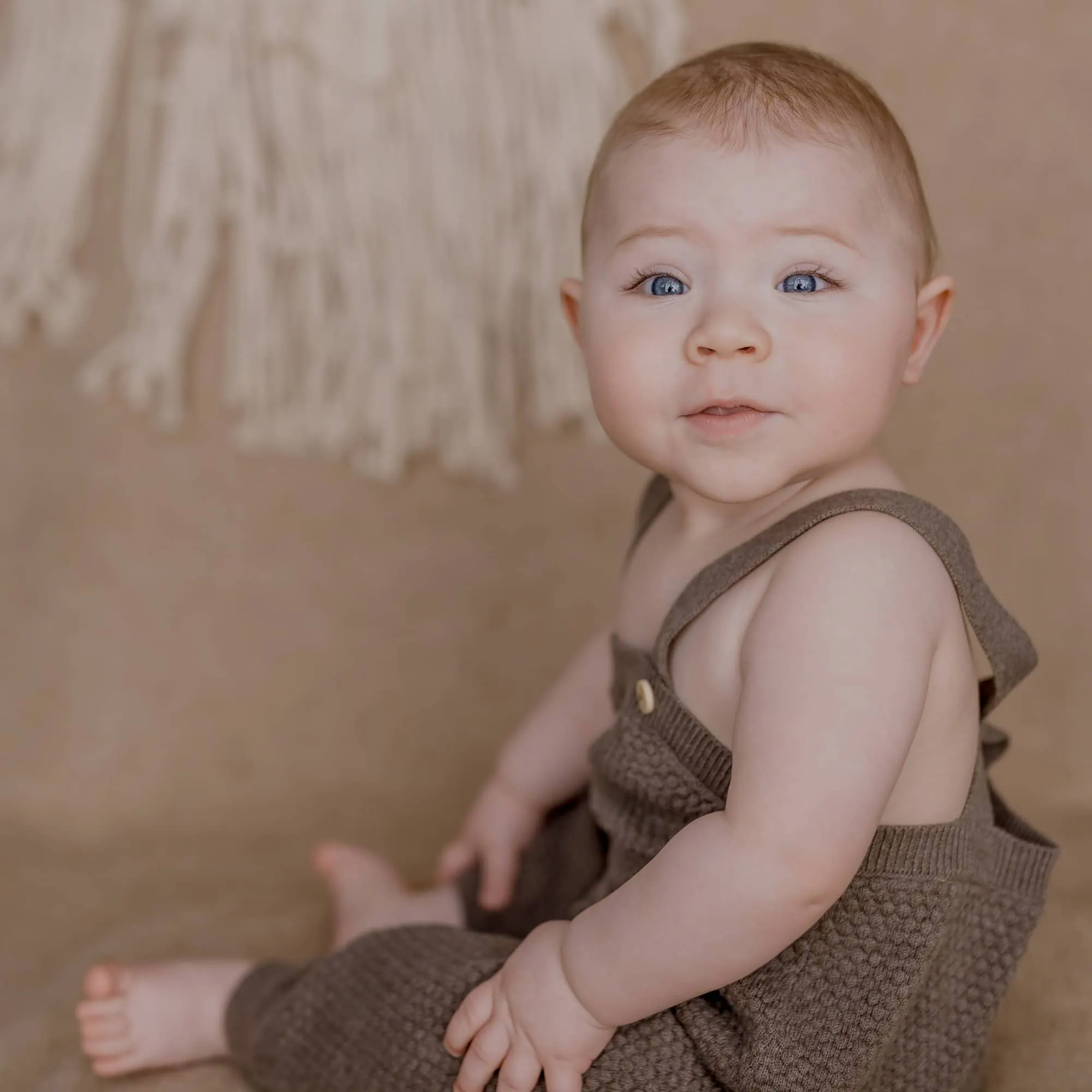 Das ist ein Bild von einem lächelnden Baby in beiger Kleidung, das sitzt.