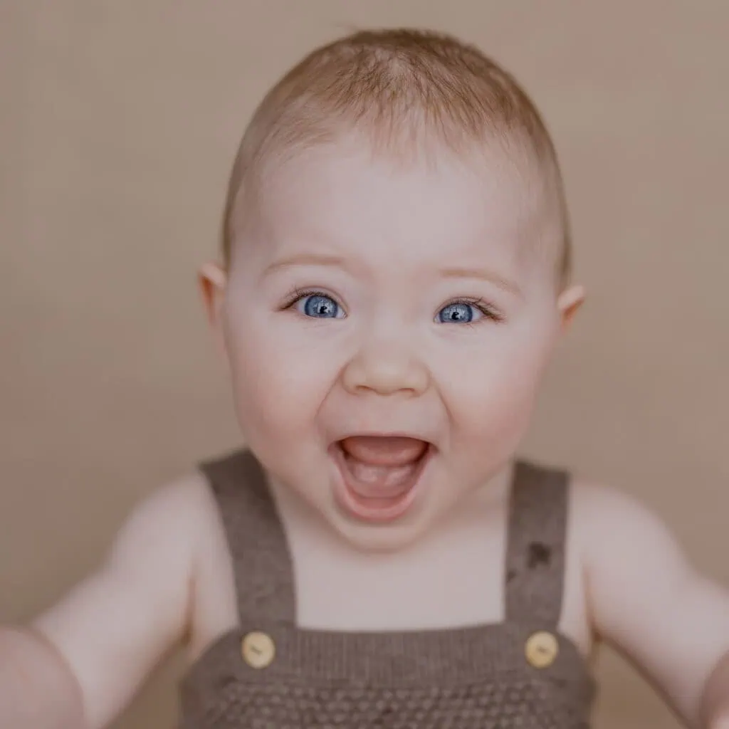 Das ist ein Bild von einem lächelnden Baby mit blauen Augen.