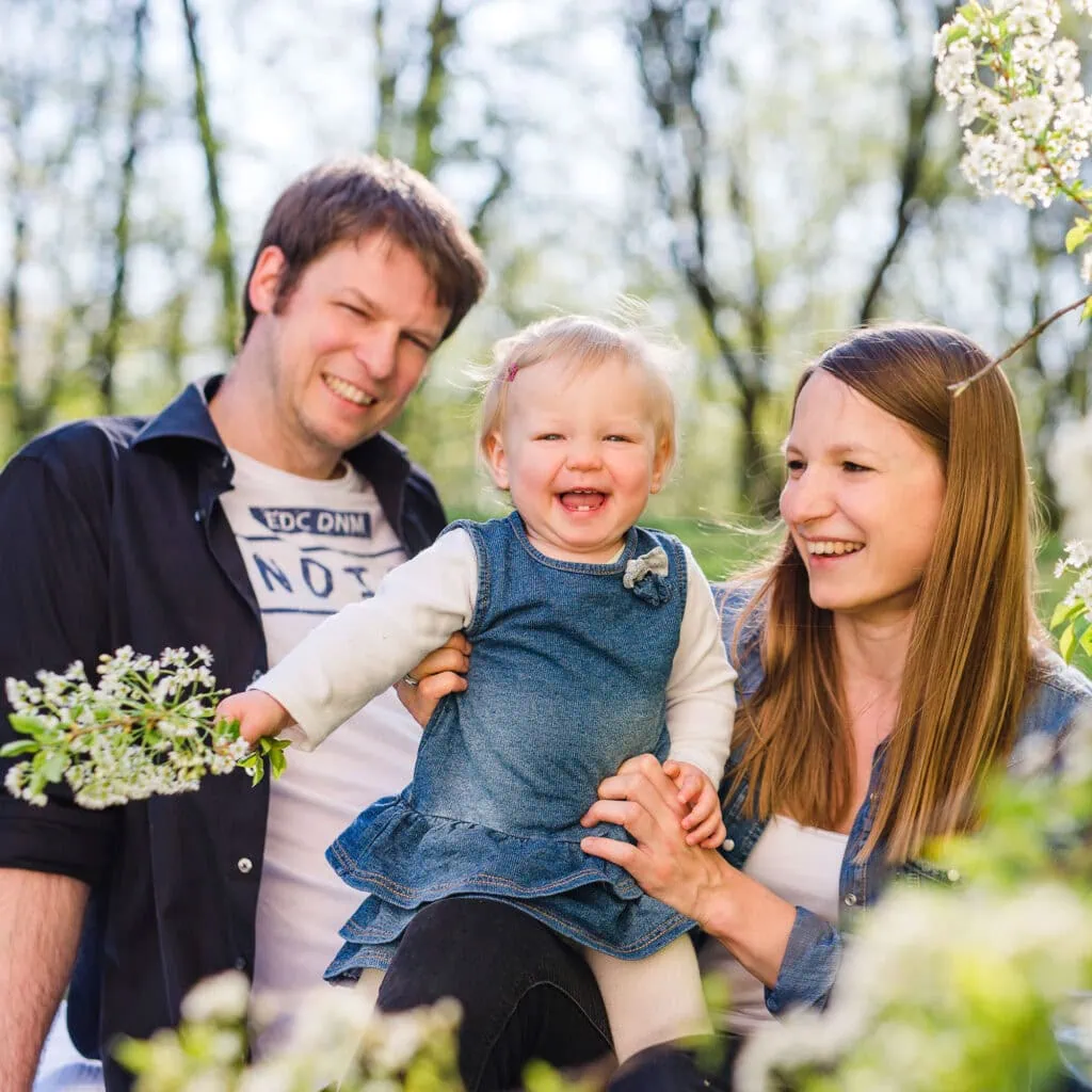 Das ist ein Bild einer glücklichen Familie mit zwei Erwachsenen und einem Kind, die draußen im Grünen sind.