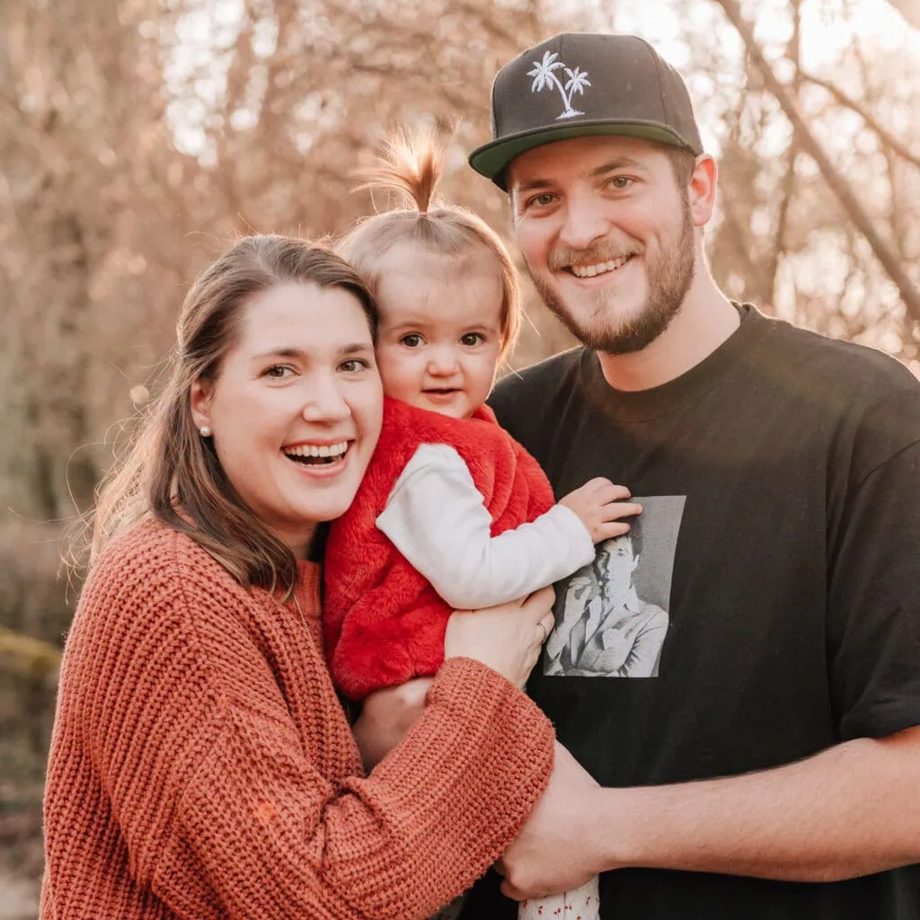 Das Bild zeigt eine Familie mit zwei Erwachsenen und einem Kleinkind, die gemeinsam lächeln.