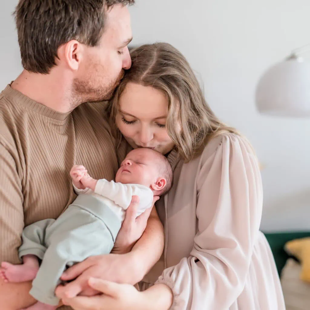 Das Bild zeigt zwei Erwachsene, die liebevoll ein Baby halten und betrachten.