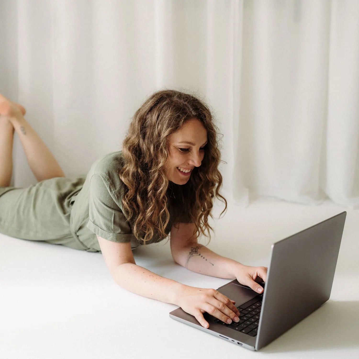 Eine lächelnde Person liegt auf dem Bauch und benutzt einen Laptop.