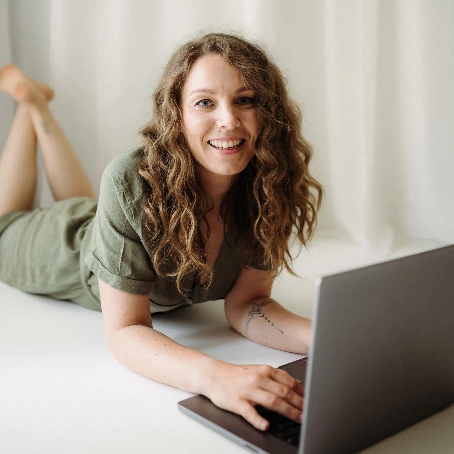 Eine lächelnde Person liegt auf dem Boden mit hochgestellten Füßen und benutzt einen Laptop.