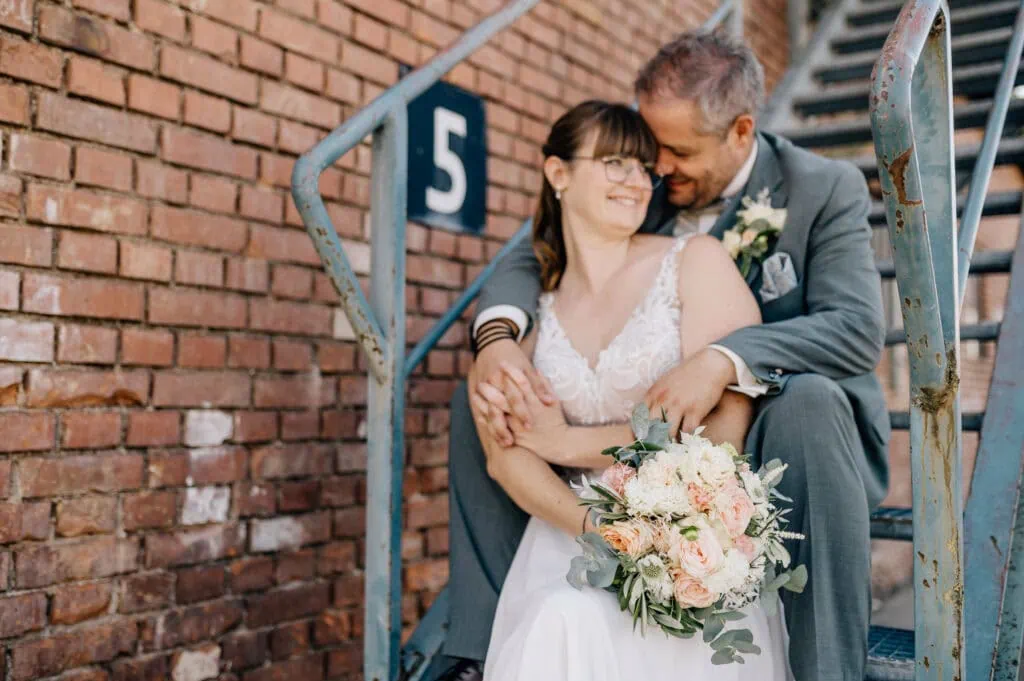 Ein glückliches Paar in Hochzeitskleidung umarmt sich auf einer Treppe.