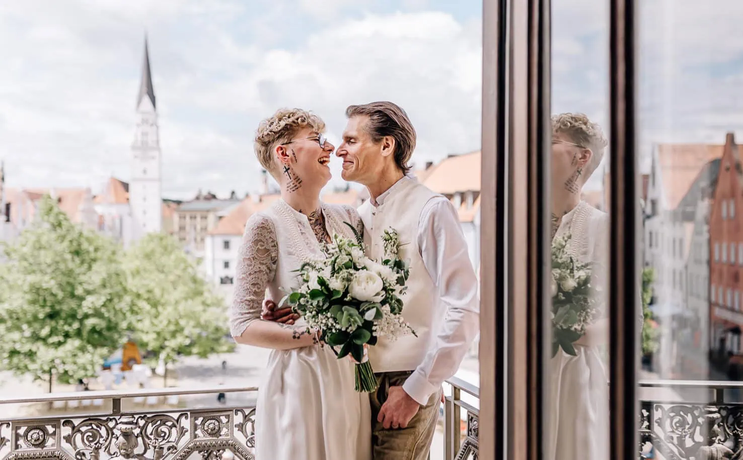 Ein Hochzeitspaar steht auf einem Balkon und blickt sich lächelnd an.