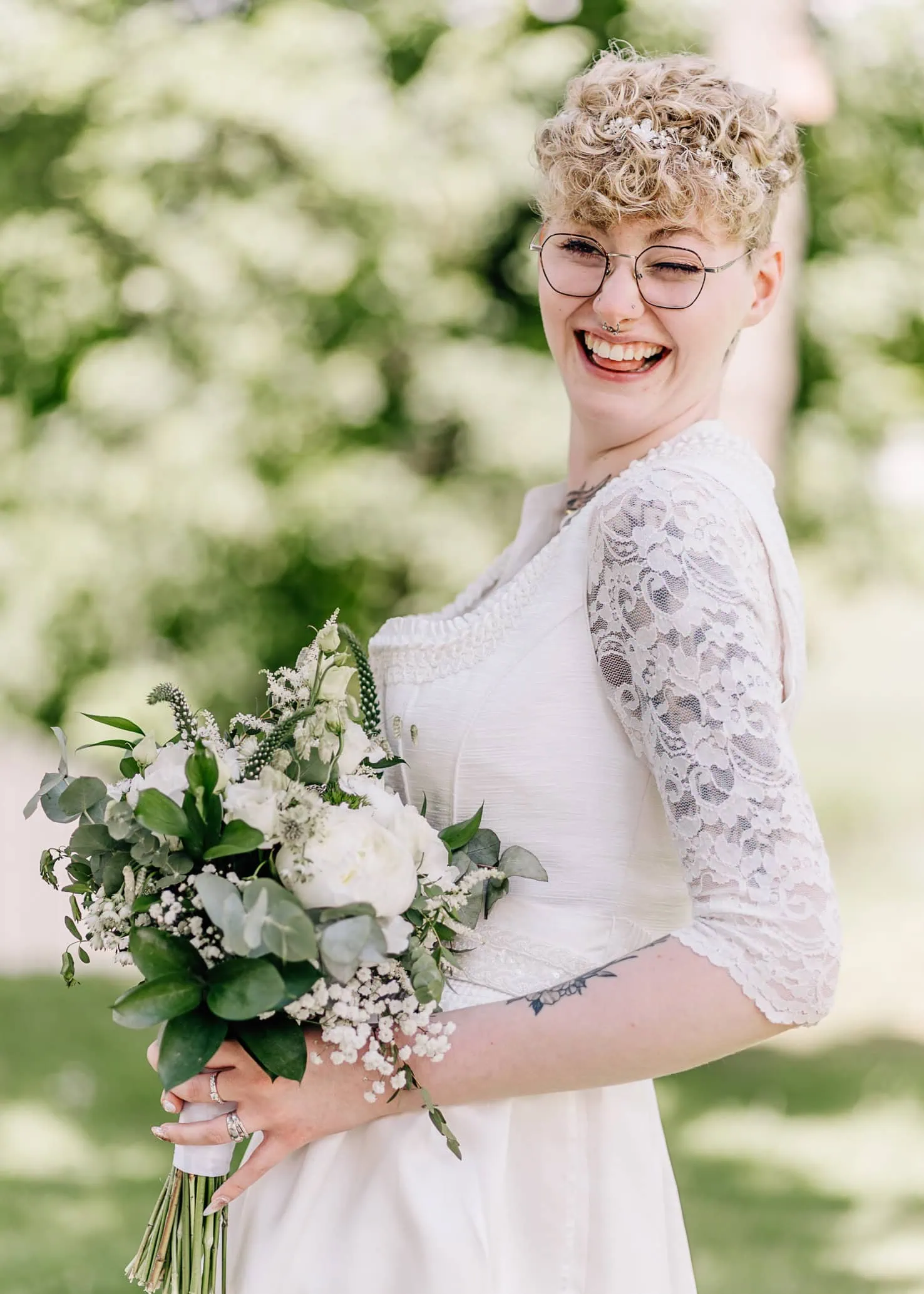 Eine lachende Person hält einen Blumenstrauß und trägt, was wie ein Hochzeitskleid erscheint.