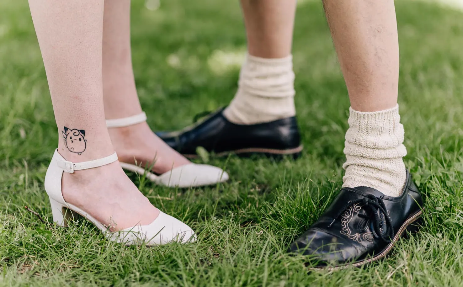 Das Bild zeigt die Beine und Füße von zwei Personen, die unterschiedliche Schuhe und Socken tragen und auf einer Rasenfläche stehen.