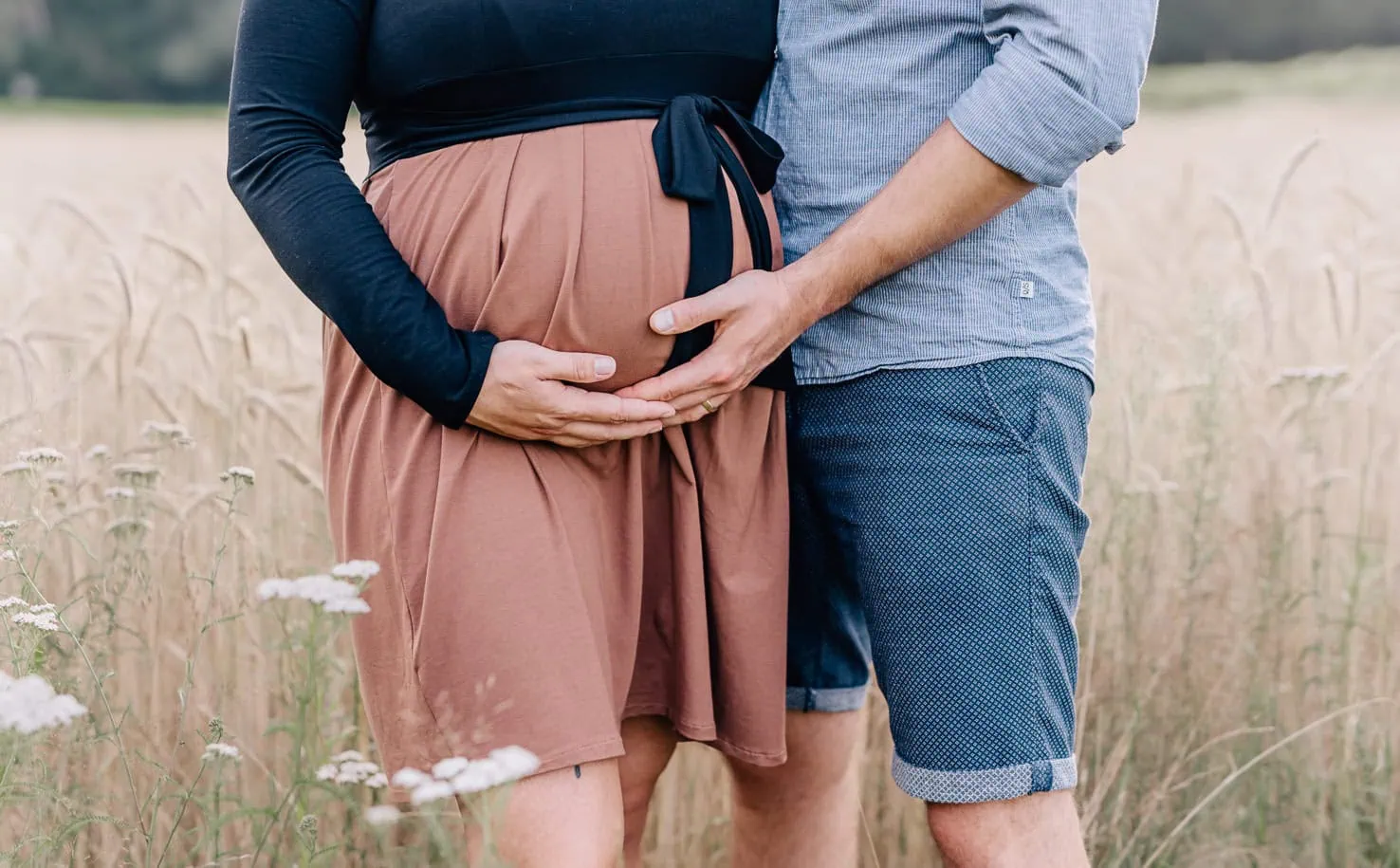 Das Bild zeigt zwei Personen, die händehaltend einen schwangeren Bauch umfassen.