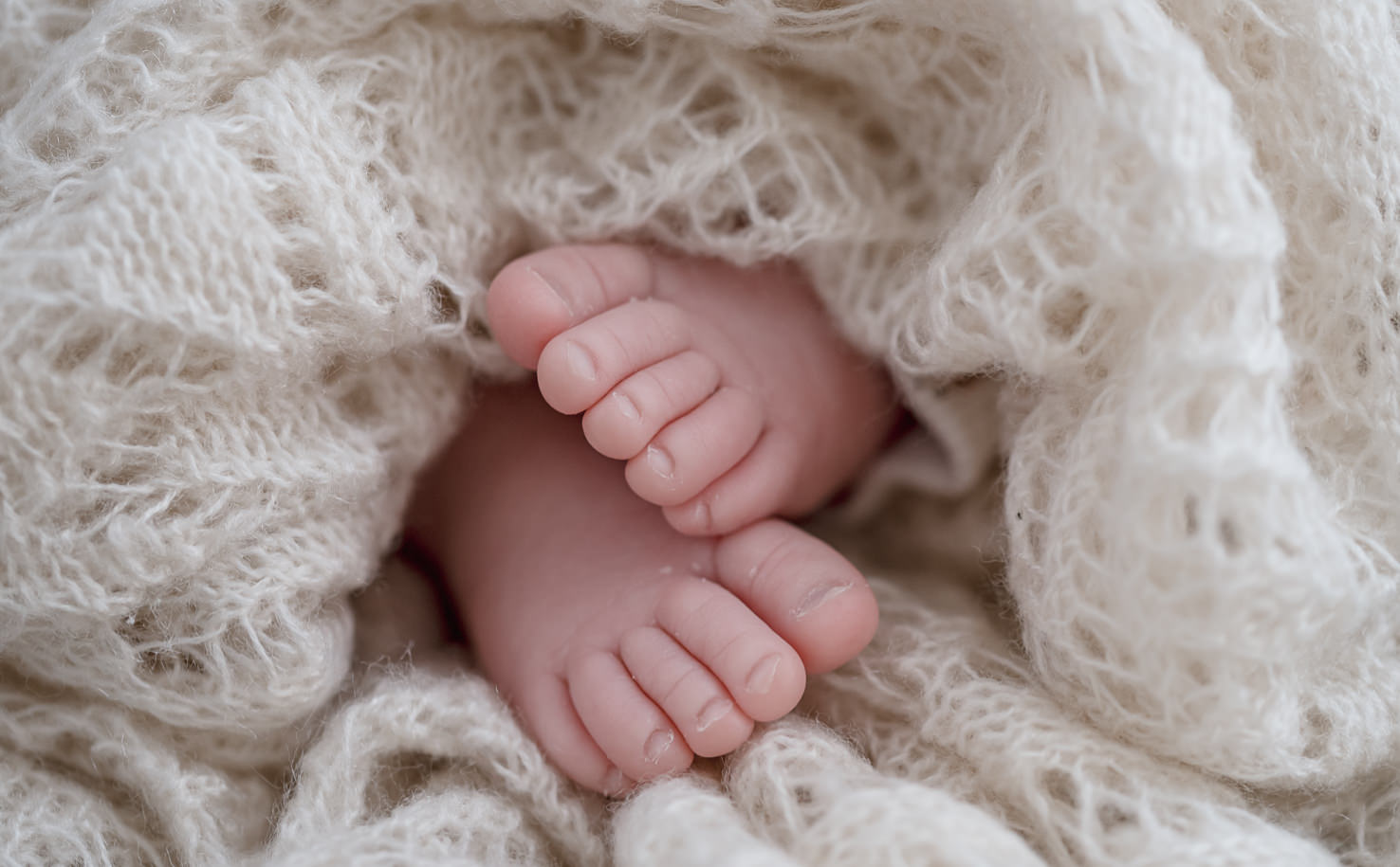 Das Bild zeigt die kleinen Füße eines Babys, die in eine weiche, wollige Decke eingehüllt sind.