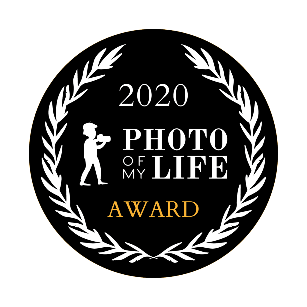 Das ist ein schwarzes, rundes Emblem mit Aufschrift "2020 PHOTO OF MY LIFE AWARD", umgeben von einem Lorbeerkranz mit einer Silhouette einer fotografierenden Person.