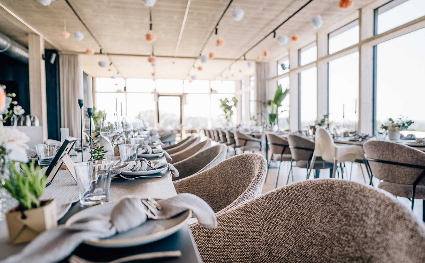 Das Bild zeigt einen elegant gedeckten Speisesaal oder Veranstaltungsraum mit Tischen, Stühlen und Dekoration.