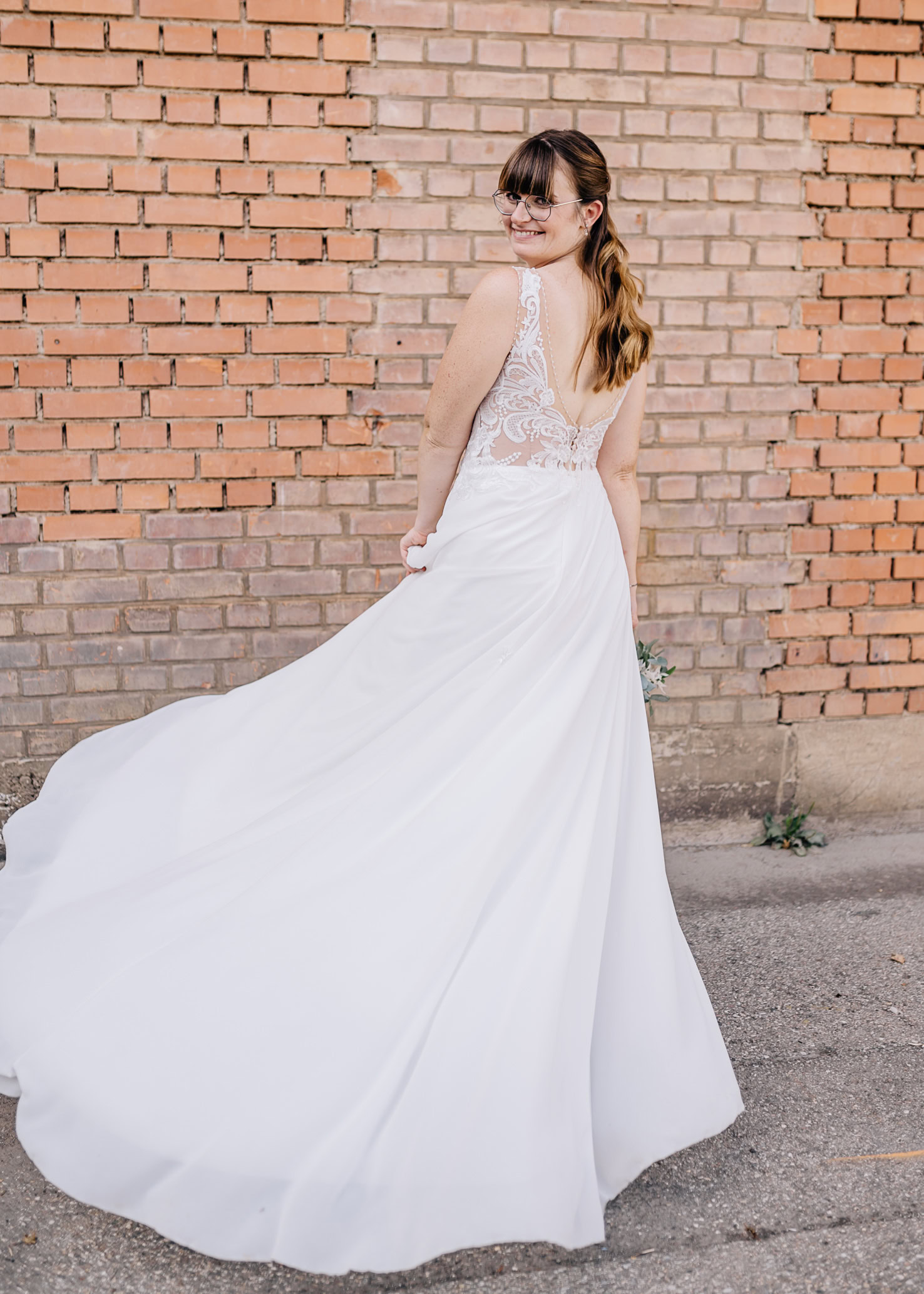 Eine Frau im Brautkleid steht vor einer Ziegelmauer.