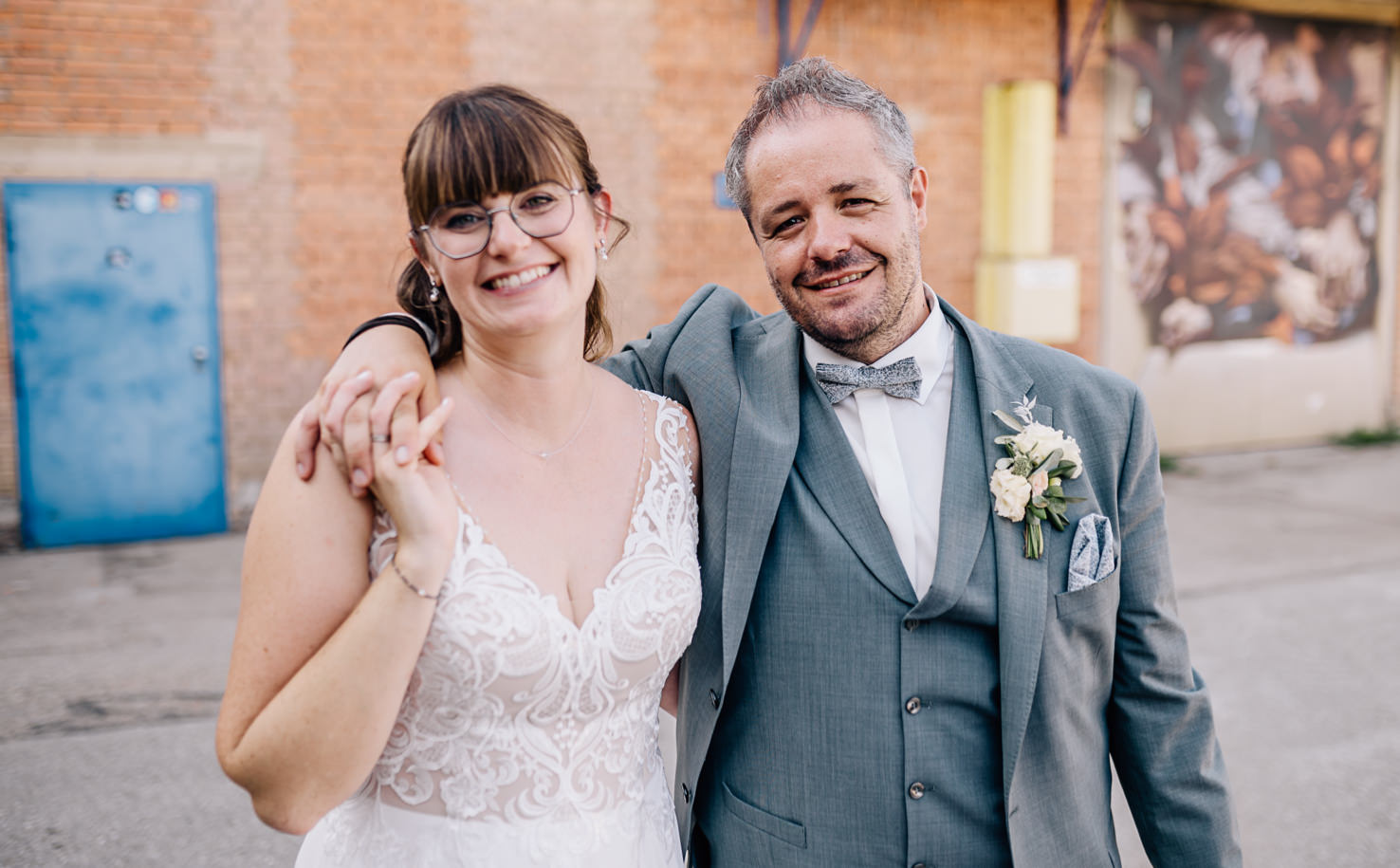 Eine Frau im Brautkleid steht vor einer Ziegelmauer.