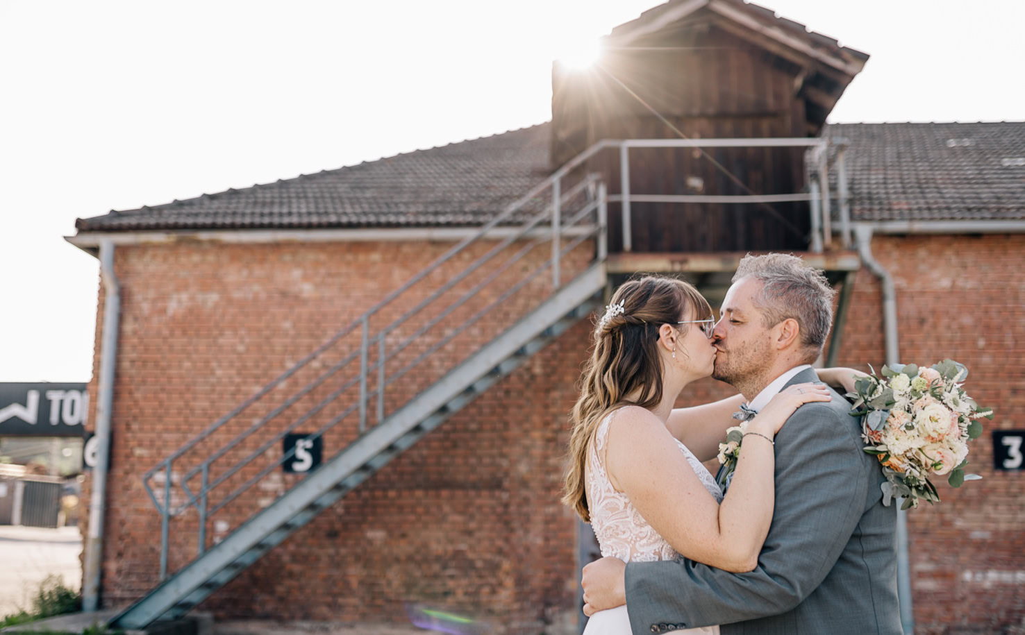 Ein Paar küsst sich vor einer alten Industriekulisse.