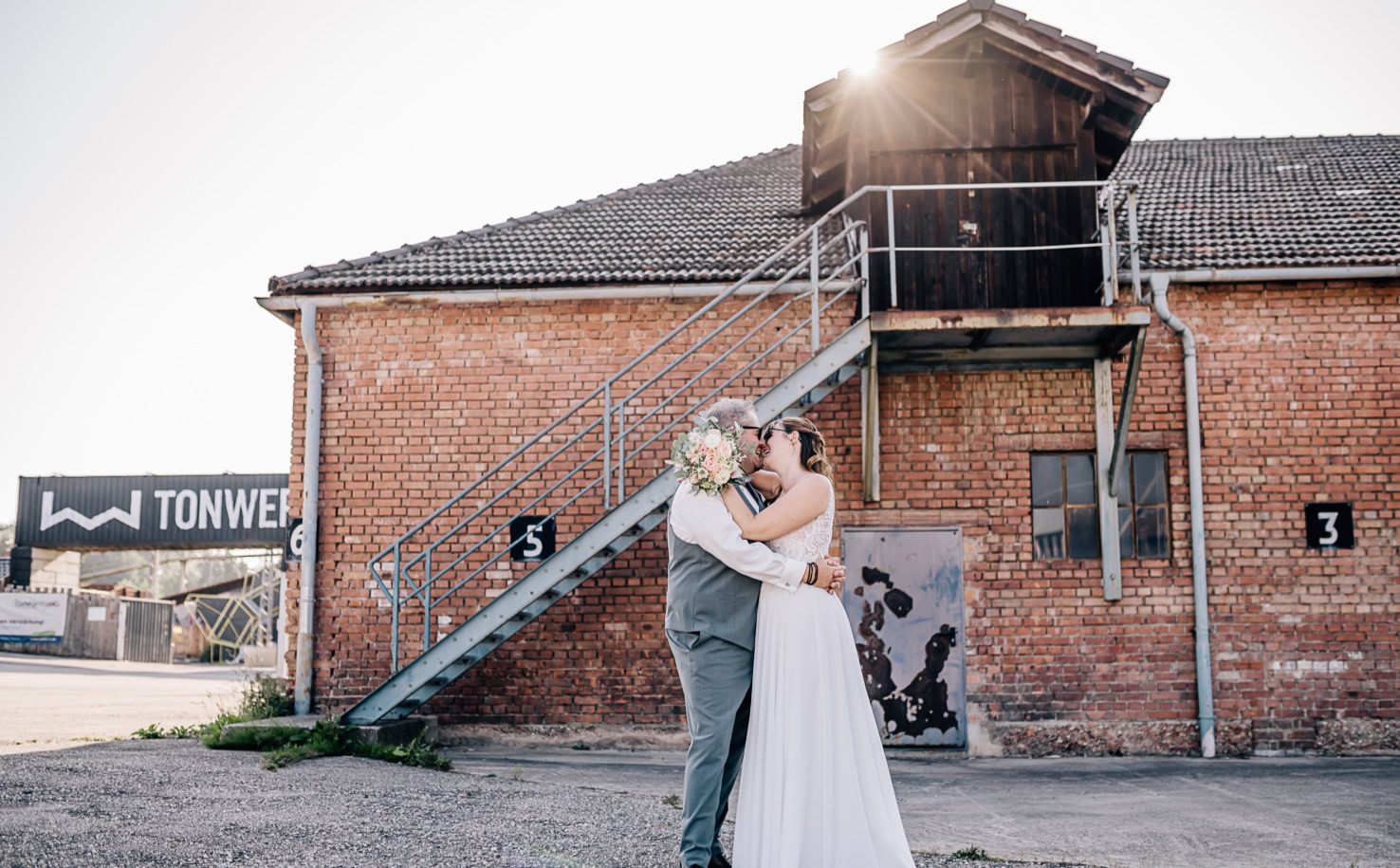 Auf dem Bild sind zwei Fotos eines Hochzeitspaares vor einer Ziegelmauer; zuerst stehen sie getrennt, dann umarmen sie sich.