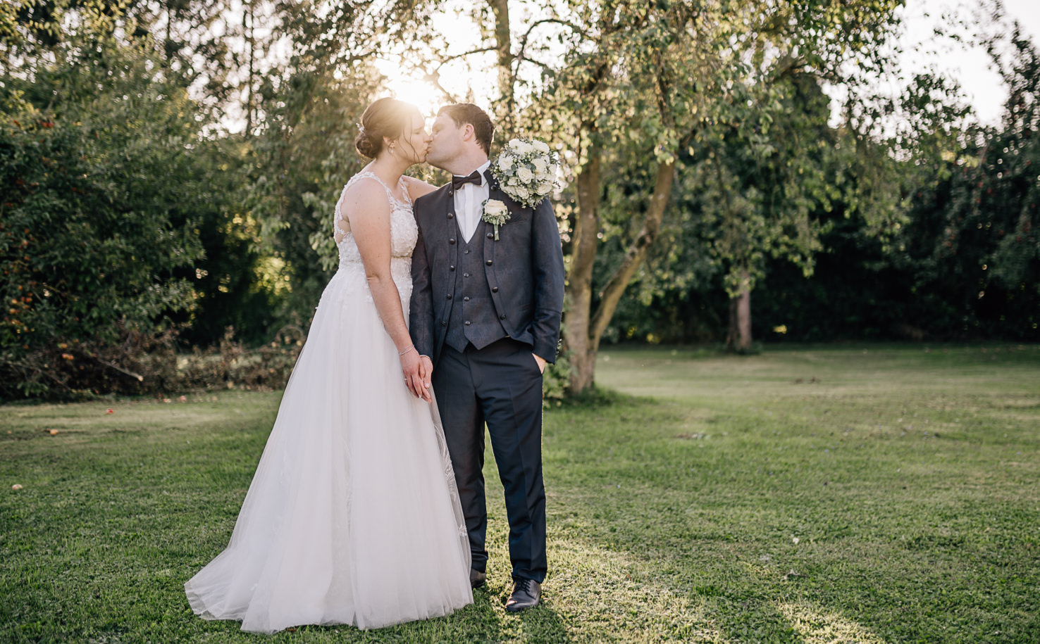 Ein Paar in Hochzeitskleidung küsst sich in einem Garten.