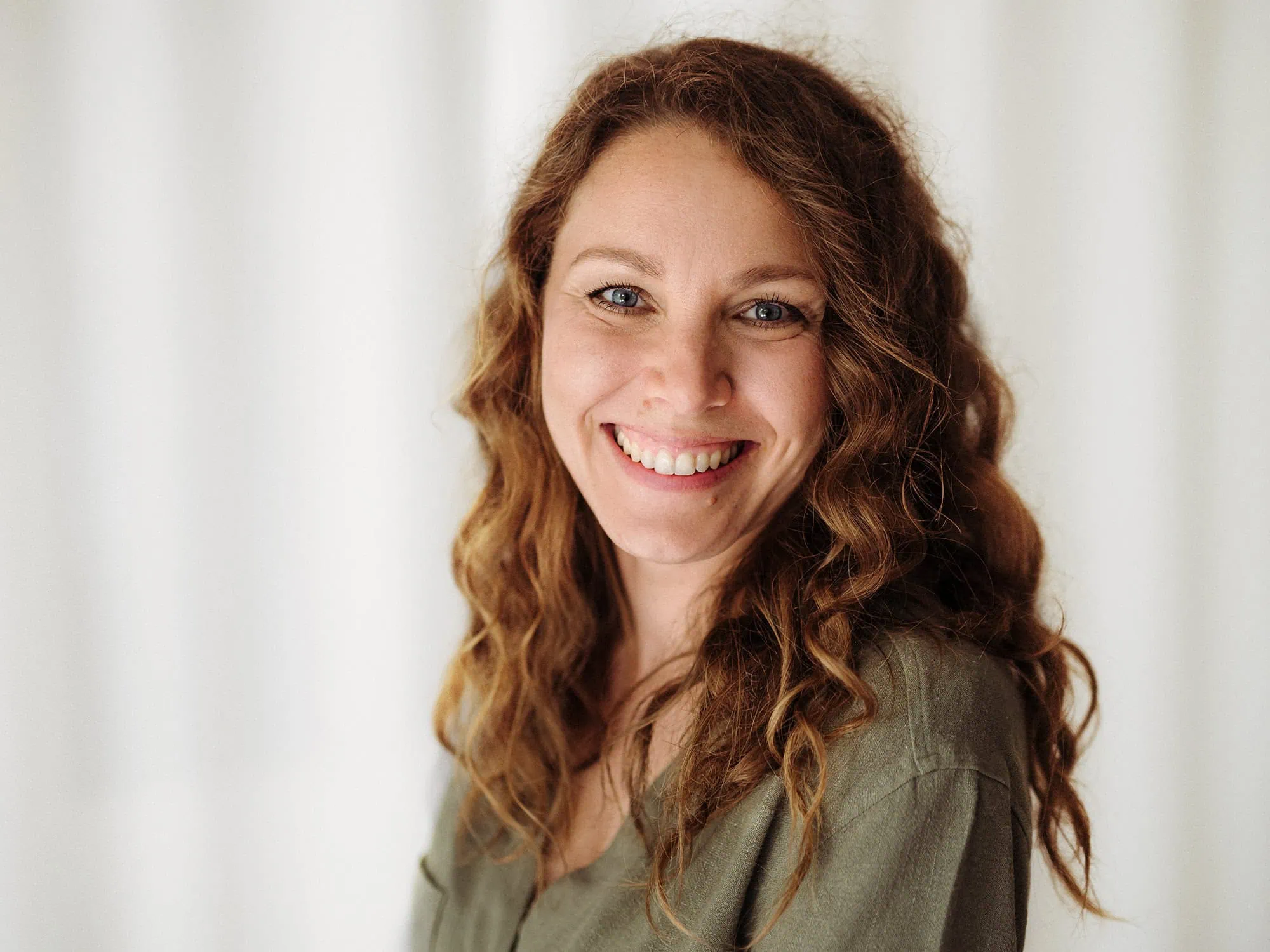 Das Portrait von Mica Zeitz fängt die natürliche Ausstrahlung und das freundliche Lächeln der Fotografin ein, ergänzt durch lockige Haare und einen entspannten Ausdruck. Ihre Professionalität und Leidenschaft für die Fotografie werden durch das weiche Licht und den neutralen Hintergrund unterstrichen, was das Bild besonders einladend wirken lässt.