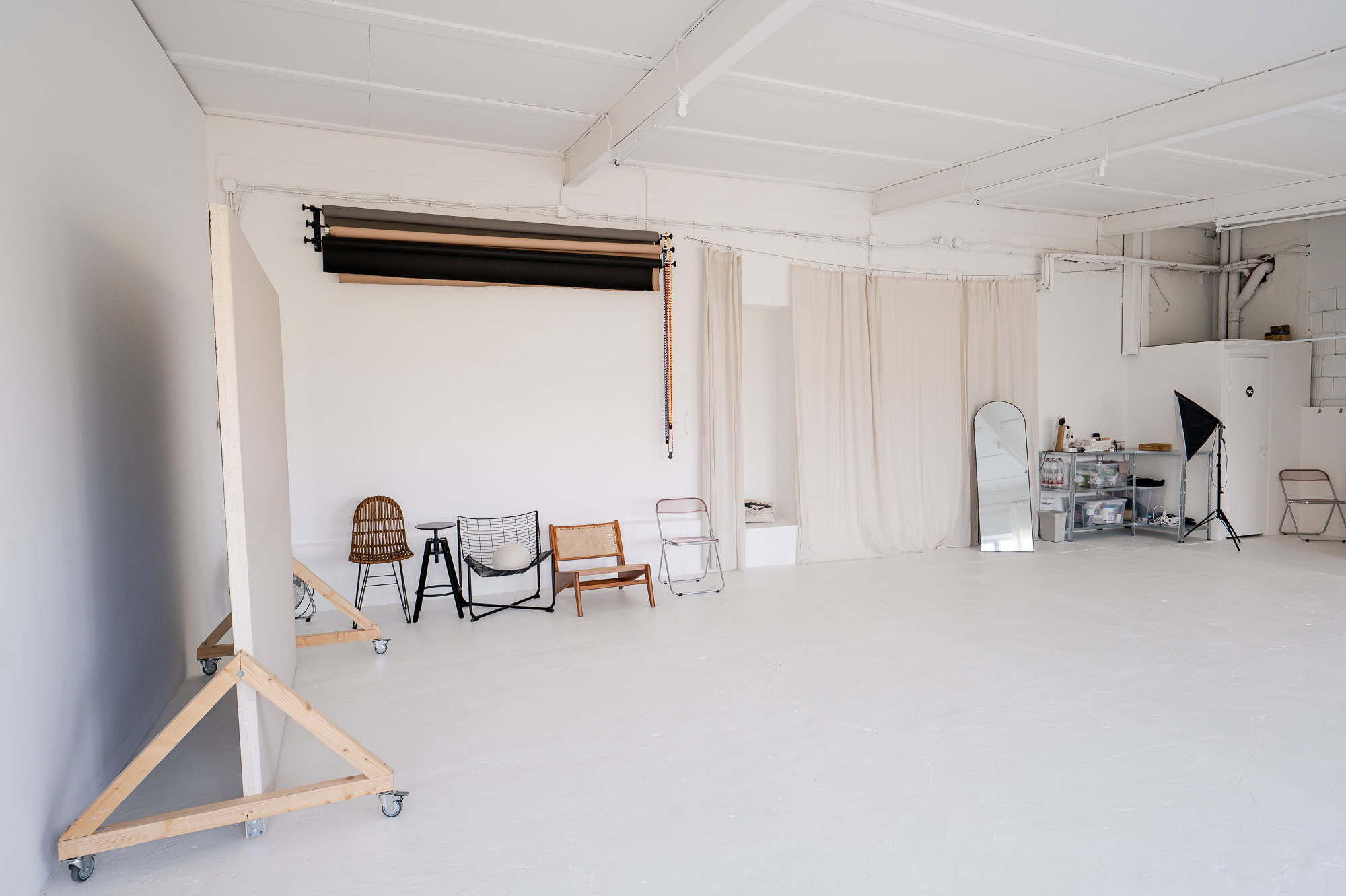 Das Bild zeigt ein helles, minimalistisches Fotostudio, ausgestattet mit verschiedenen Sitzgelegenheiten und hochwertigem Licht-Equipment, ideal für kreative Fotoprojekte. Fotografiert von Mica Zeitz, verkörpert der Raum eine harmonische Ästhetik, die sich perfekt für professionelle Portrait- und Produktfotografie eignet.