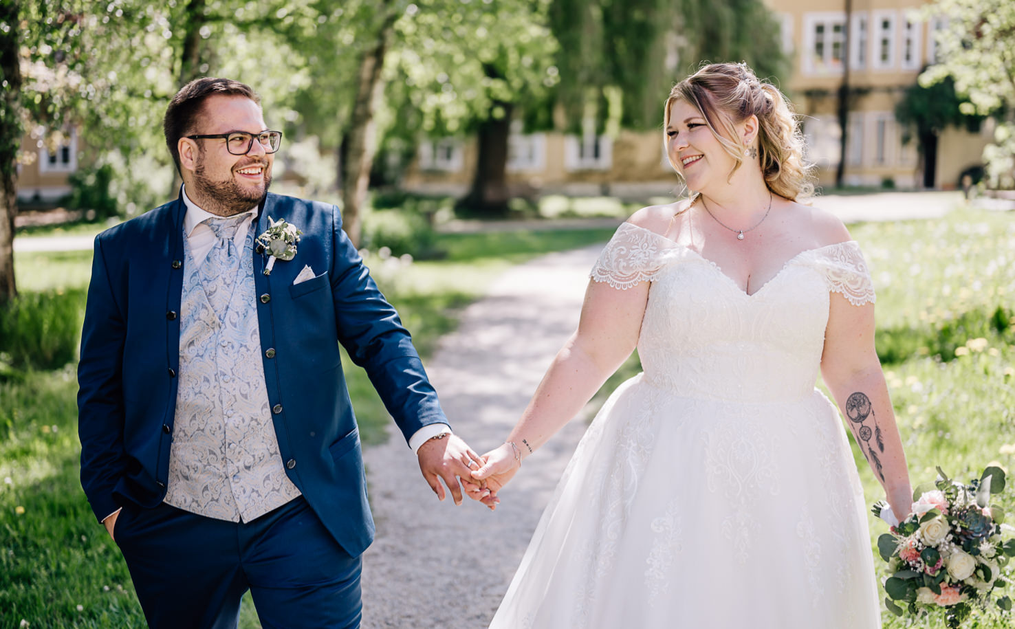 Das romantische Hochzeitsfoto, aufgenommen von der talentierten Fotografin Mica Zeitz, fängt das glückliche Brautpaar beim Händchenhalten in einer malerischen Gartenlandschaft ein. Die strahlenden Gesichter und der traumhafte Brautstrauß verleihen diesem Bild eine unvergessliche Atmosphäre voller Liebe und Freude.
