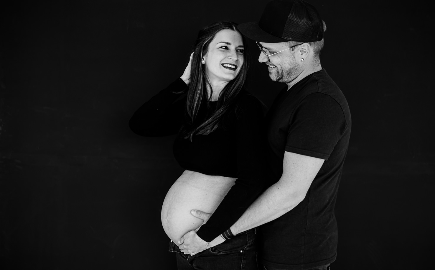 Dieses wunderschöne schwarz-weiße Bild, aufgenommen von der Fotografin Mica Zeitz, zeigt ein glückliches Paar in einer intimen Momentaufnahme während der Schwangerschaft. Die emotionale Verbindung und die liebevolle Berührung des Bauches symbolisieren Freude und Vorfreude auf das kommende Leben.