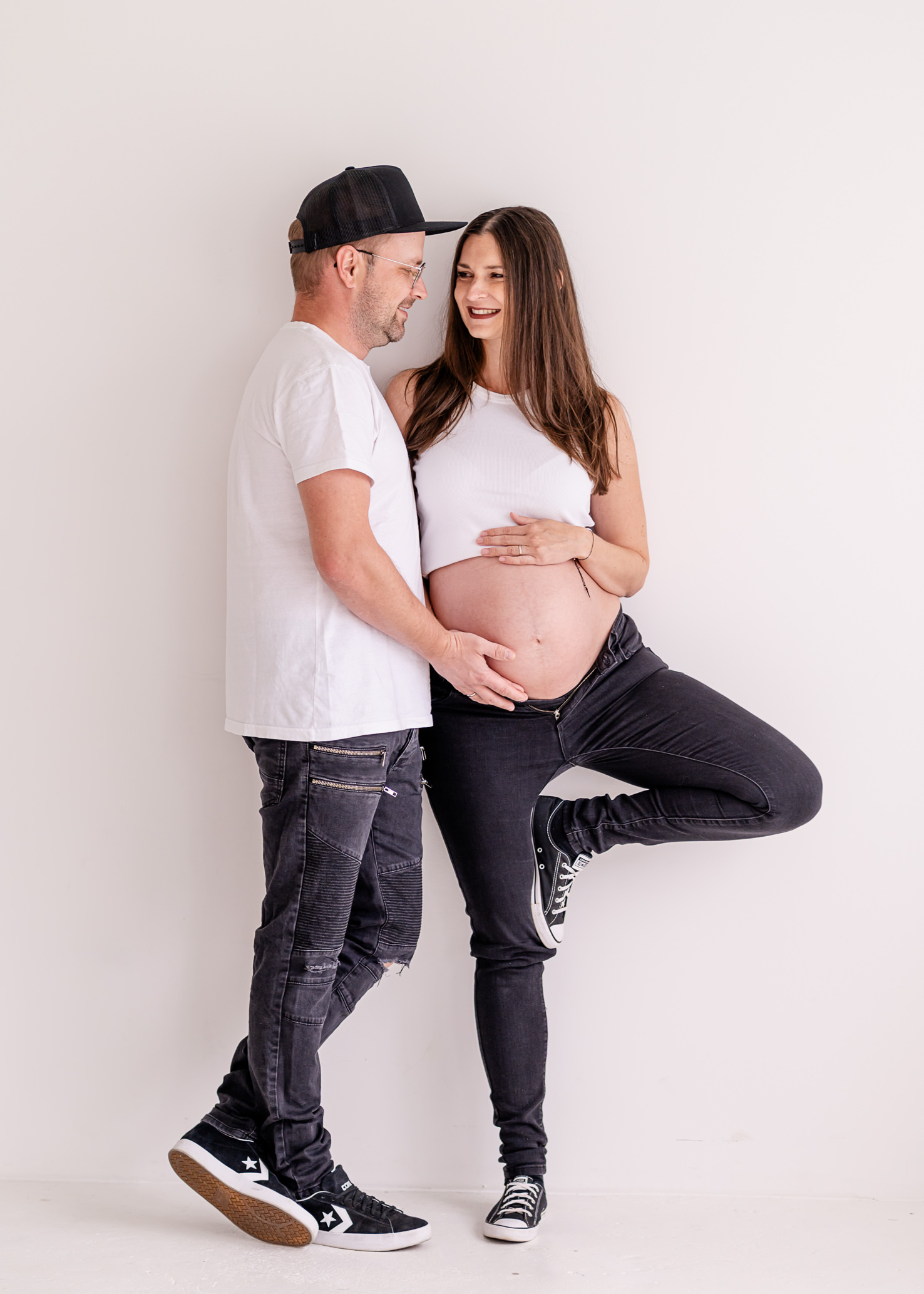 In diesem liebevollen Schwangerschaftsbild, festgehalten von der Fotografin Mica Zeitz, strahlen ein werdendes Elternpaar in lässiger Kleidung zusammen Freude und Vorfreude auf ihr Baby aus. Die harmonische Pose und der helle Hintergrund unterstreichen die emotionale Verbindung und die Schönheit der Schwangerschaft.