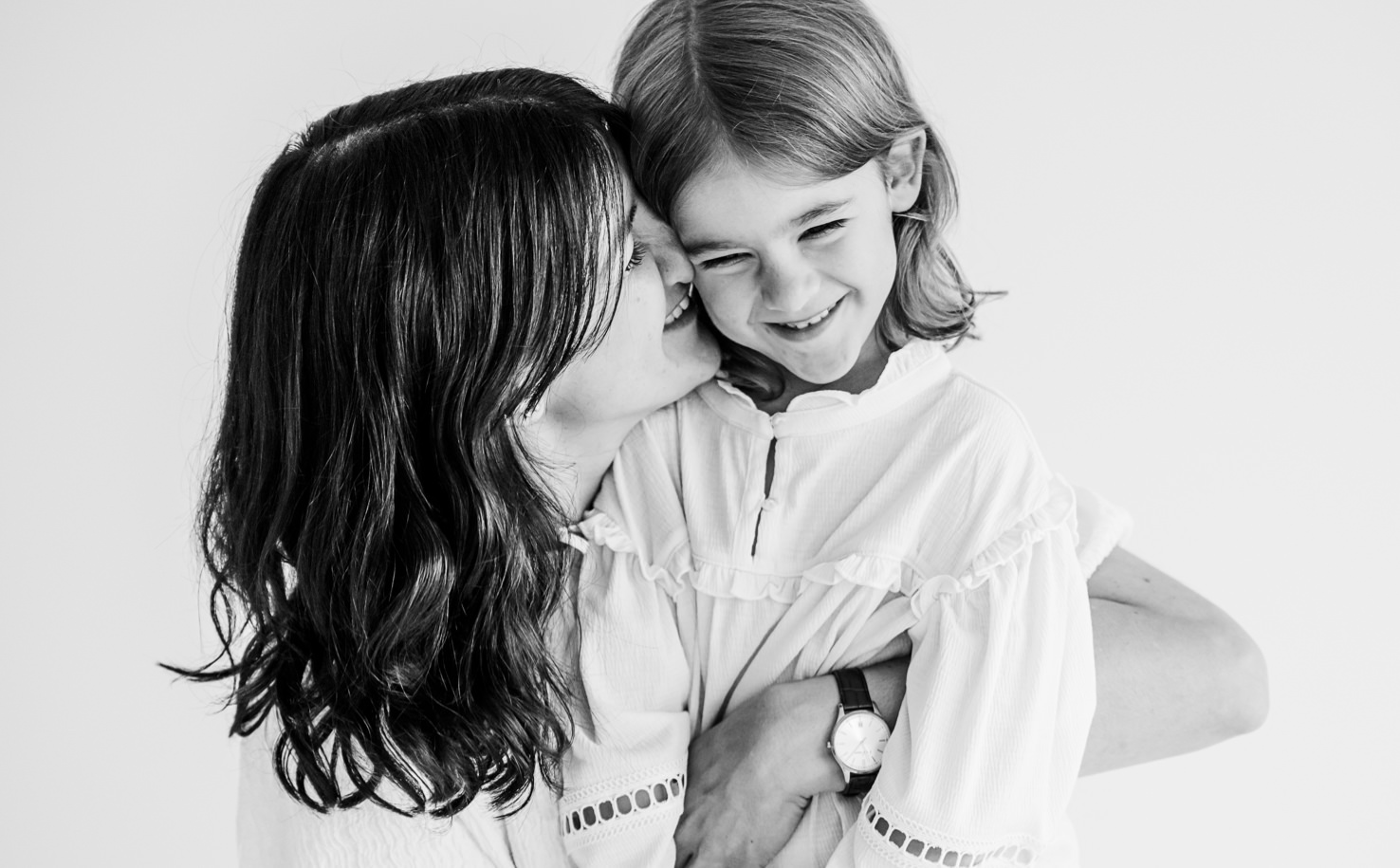 Dieses bezaubernde Schwarz-Weiß-Foto von Mica Zeitz zeigt eine herzliche Momentaufnahme zwischen Mutter und Tochter, die von Liebe und Freude geprägt ist. Die innige Umarmung und das Lächeln der beiden verleihen dem Bild eine besondere Wärme, ideal für natürliche Familienfotografie.