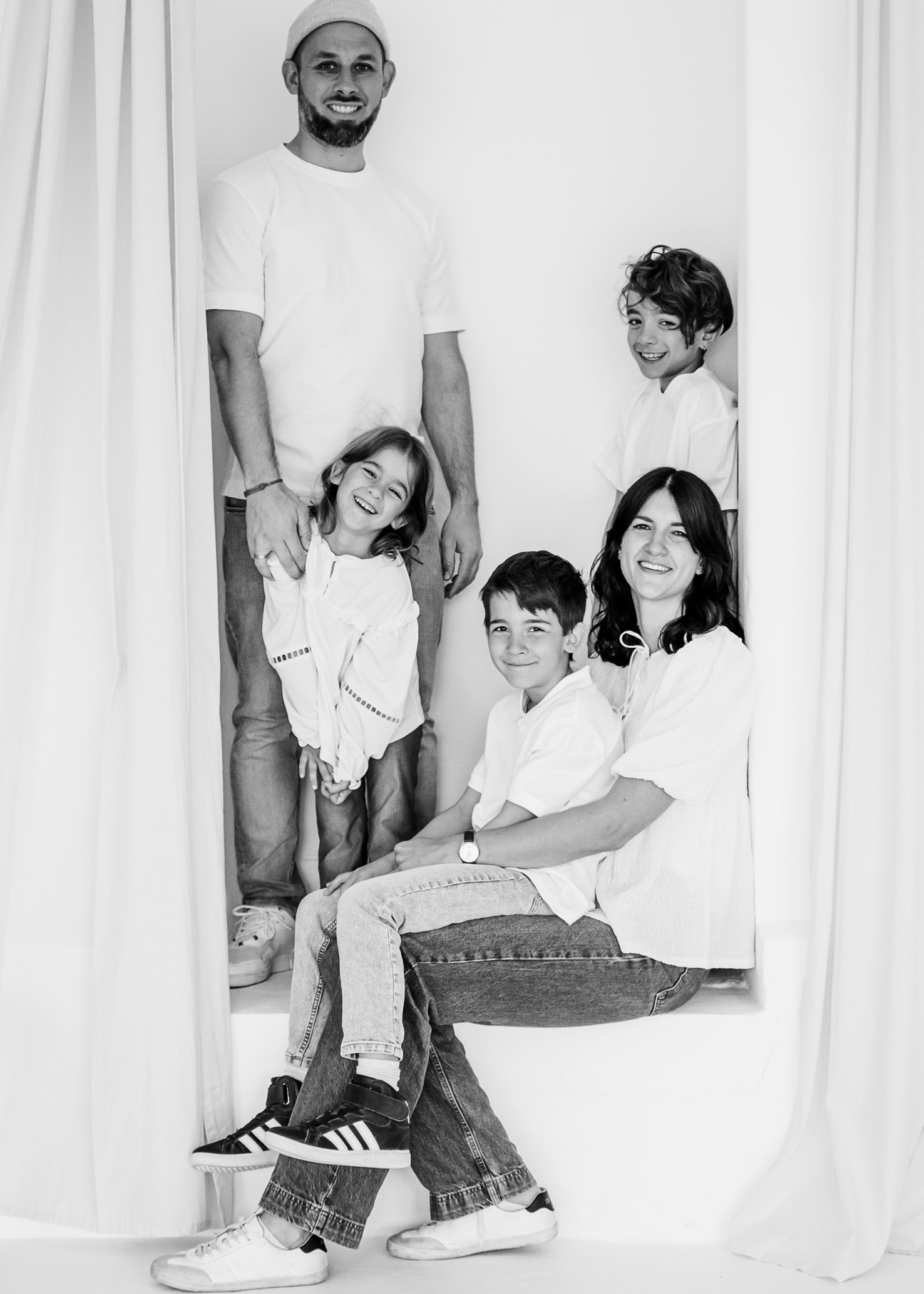 In einem stylischen, hellen Innenraum zeigt das Familienporträt von Fotografin Mica Zeitz eine herzliche und lebendige Momentaufnahme, die pure Freude und Verbundenheit ausstrahlt. Die Kinder posieren fröhlich und die Eltern strahlen Liebe und Zufriedenheit in einem unkomplizierten, modernen Look aus.