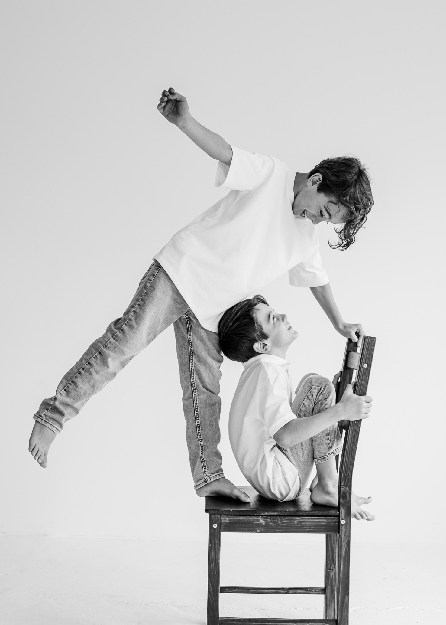 Das ausdrucksstarke Schwarz-Weiß-Foto von Mica Zeitz zeigt zwei spielende Kinder, die ihre Unbeschwertheit und Freude ausleben, während sie kreativ mit einer Holzstuhl-Posing spielen. Die dynamische Komposition fängt den Moment voller Lebensfreude und kindlicher Entdeckung ein, perfekt für Familienfotografie und emotionale Erinnerungen.