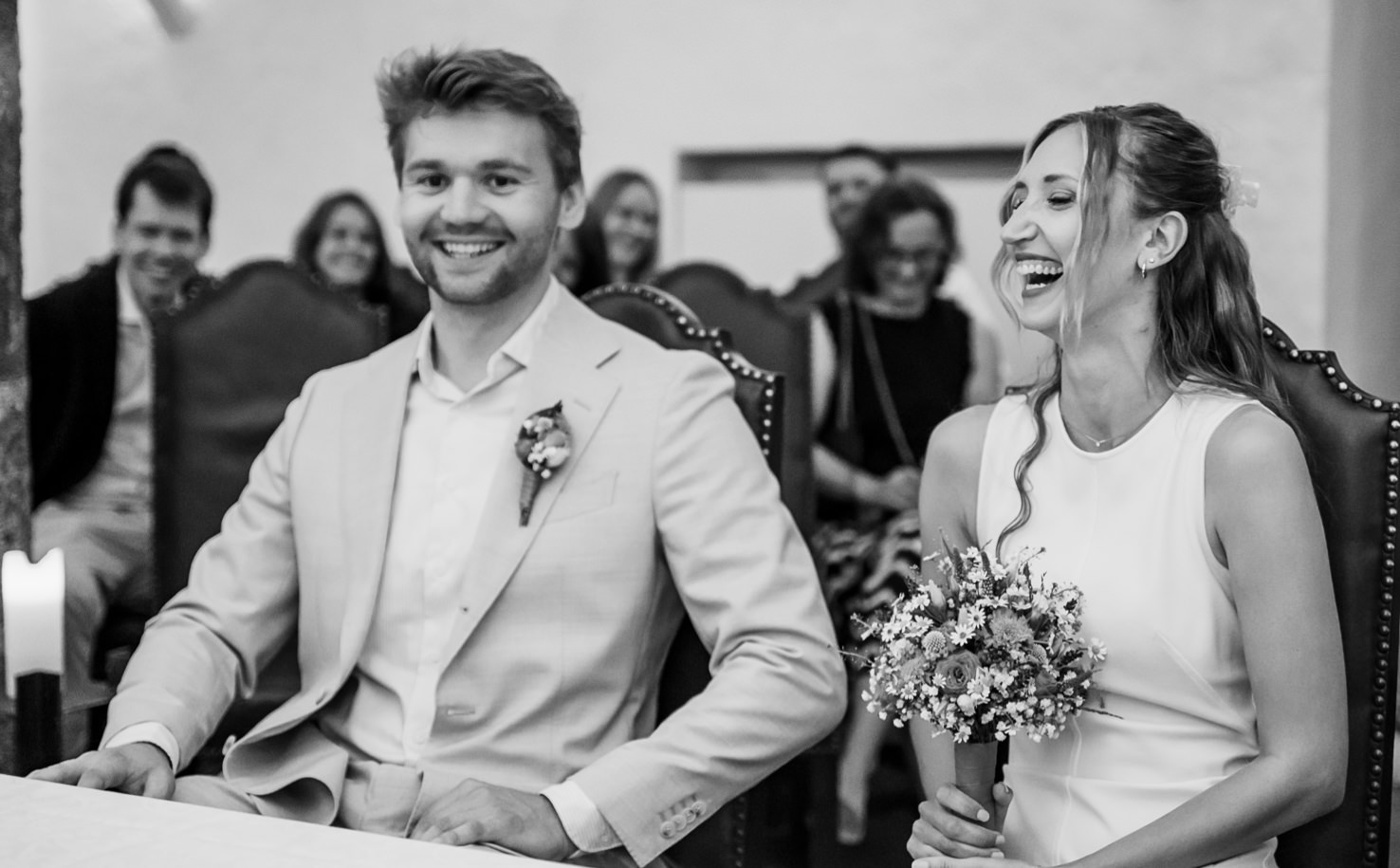 Dieses emotionale Hochzeitsfoto von Mica Zeitz fängt den unbeschwerten Moment eines lächelnden Paares während seiner Zeremonie ein, umgeben von einer fröhlichen Gesellschaft. Die Kombination aus liebevollen Blicken und Lachen schafft eine intime Atmosphäre, die die Freude des besonderen Tages perfekt widerspiegelt.