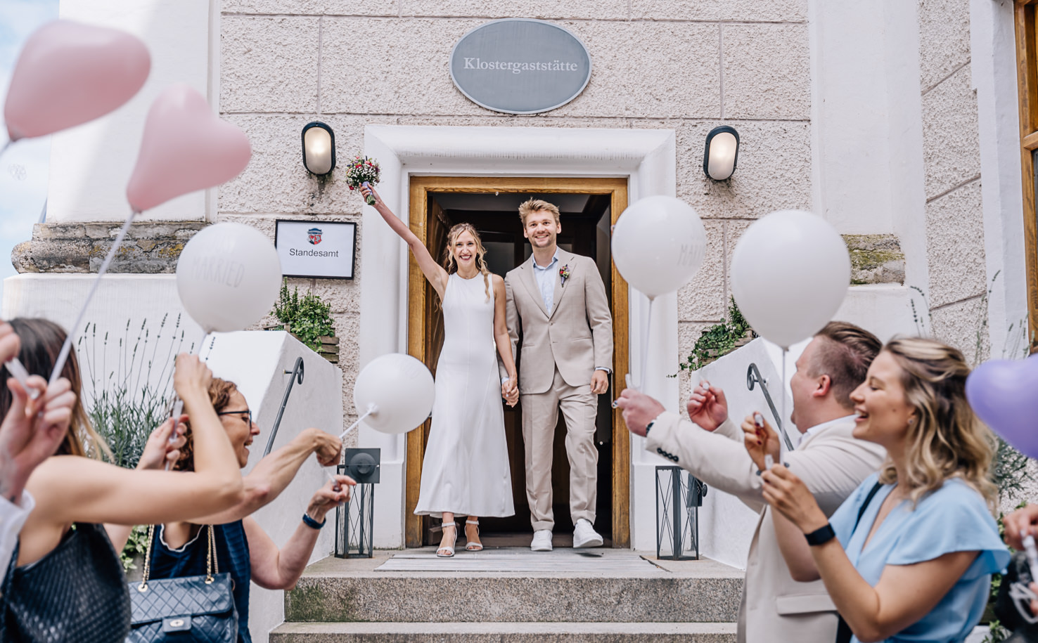 Das Bild zeigt ein fröhliches Brautpaar, das nach der Trauung am Standesamt von Freunden mit Luftballons gefeiert wird. Captured by Fotografin Mica Zeitz, strahlt die Szene Freude und Glück aus, ideal für Hochzeits- und Eventfotografie.