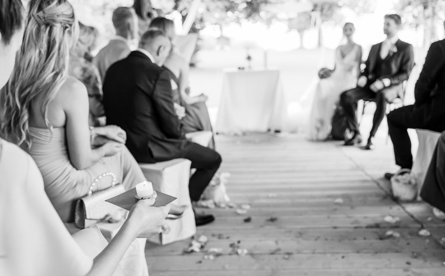Das Bild von Mica Zeitz fängt den emotionalen Moment einer Hochzeit ein, bei dem die Gäste gespannt auf das Brautpaar blicken. Die schwarz-weiße Fotografie unterstreicht die intime Atmosphäre und die Zeremonie des ewigen Versprechens.