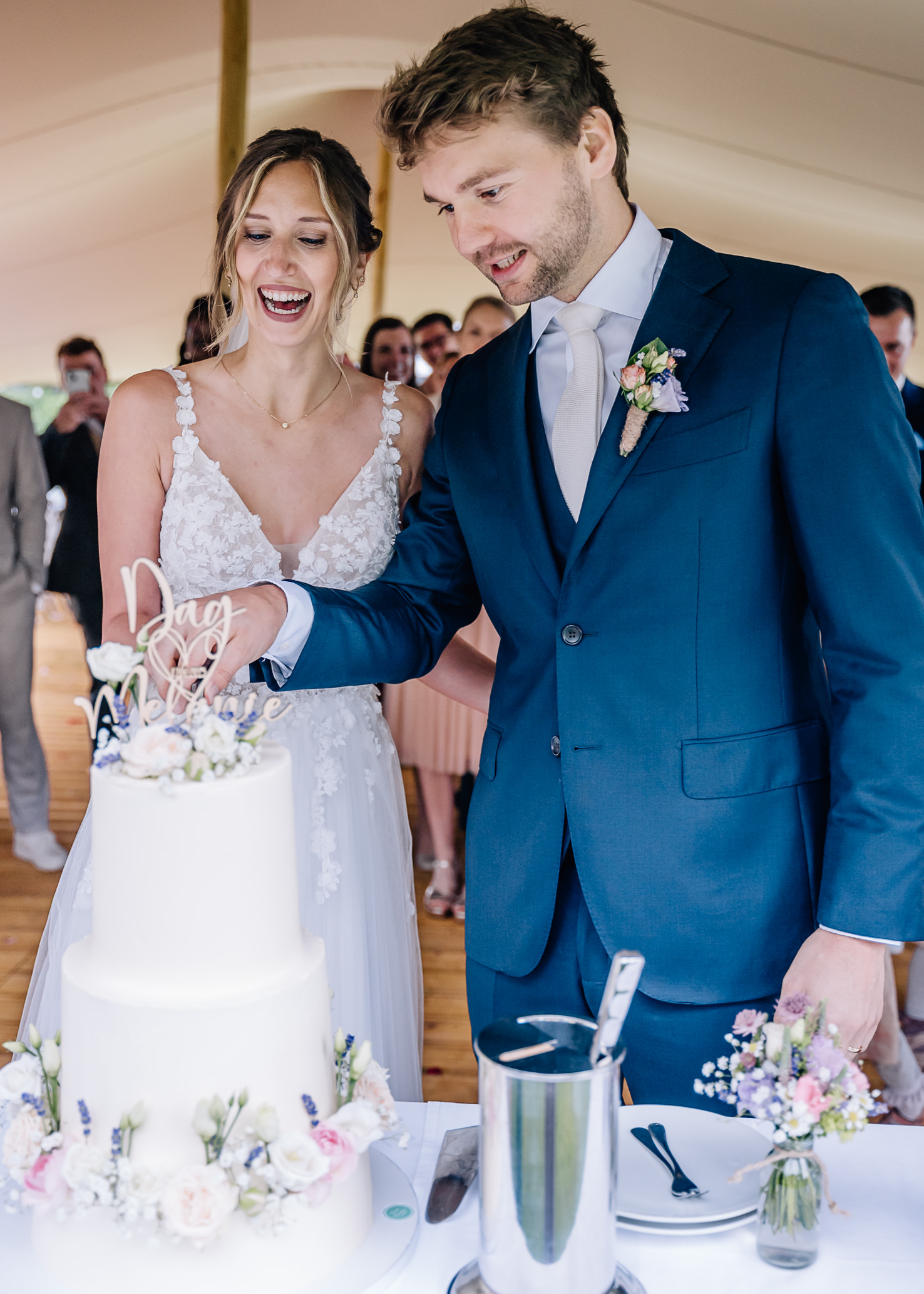 Ein strahlendes Brautpaar schneidet voller Freude ihre traumhafte Hochzeitstorte an, während ein elegantes und festliches Ambiente die Szene umgibt. Dieses besondere Momentfoto wurde von der talentierten Fotografin Mica Zeitz festgehalten und fängt die Emotionen und die festliche Stimmung perfekt ein.