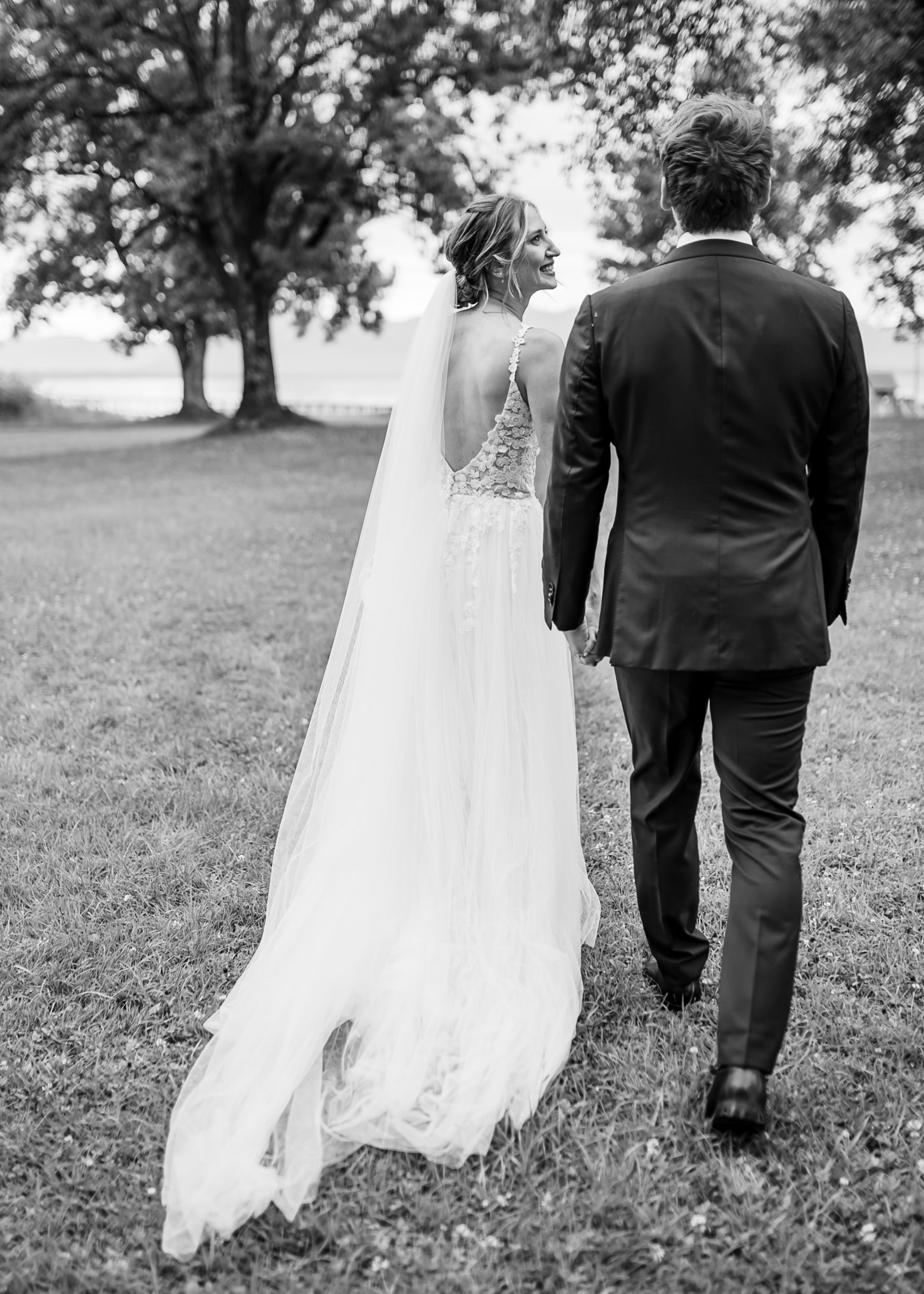 Das Bild von Mica Zeitz zeigt ein romantisches Paar, das Hand in Hand in einer malerischen Landschaft spaziert, während der frische Wind die Brautkleid-Schnellbewegung sanft umspielt. Die natürliche Kulisse und die Emotionen des Moments fangen die Essenz eines unvergesslichen Hochzeitstags perfekt ein.