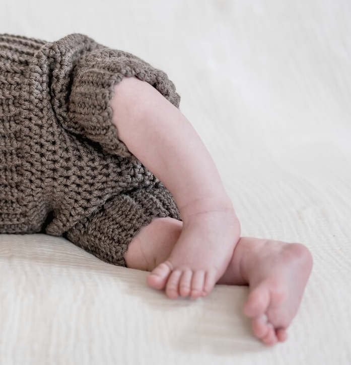 Das entzückende Bild von Mica Zeitz zeigt zarte Babyfüße und einen kleinen Arm in einem handgestrickten Outfit, die die Unschuld und Freude der frühen Kindheit verkörpern. Diese Fotografie verbindet liebevolle Details mit einem minimalistischen Hintergrund und fängt die süßen Momente des Babylebens perfekt ein.
