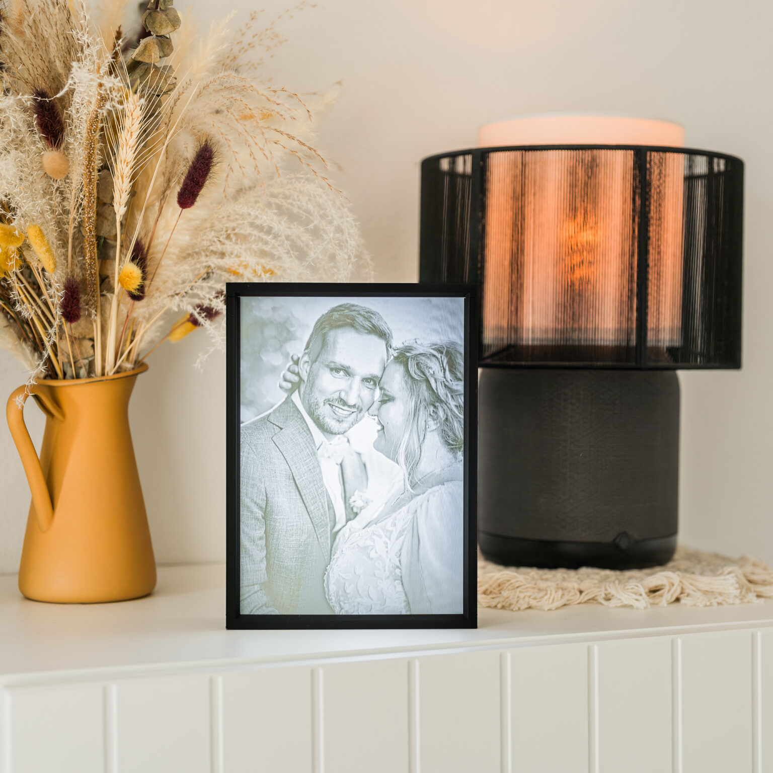 Das stimmungsvolle Bild zeigt ein liebevolles Paar in einem eleganten Rahmen, umgeben von stilvollem Interieur mit einer dekorativen Vase und einer modernen Lampe. Fotografiert von Mica Zeitz, vermittelt das Werk romantische Atmosphäre und zeitlose Eleganz, ideal für Hochzeits- und Paarfotografie.