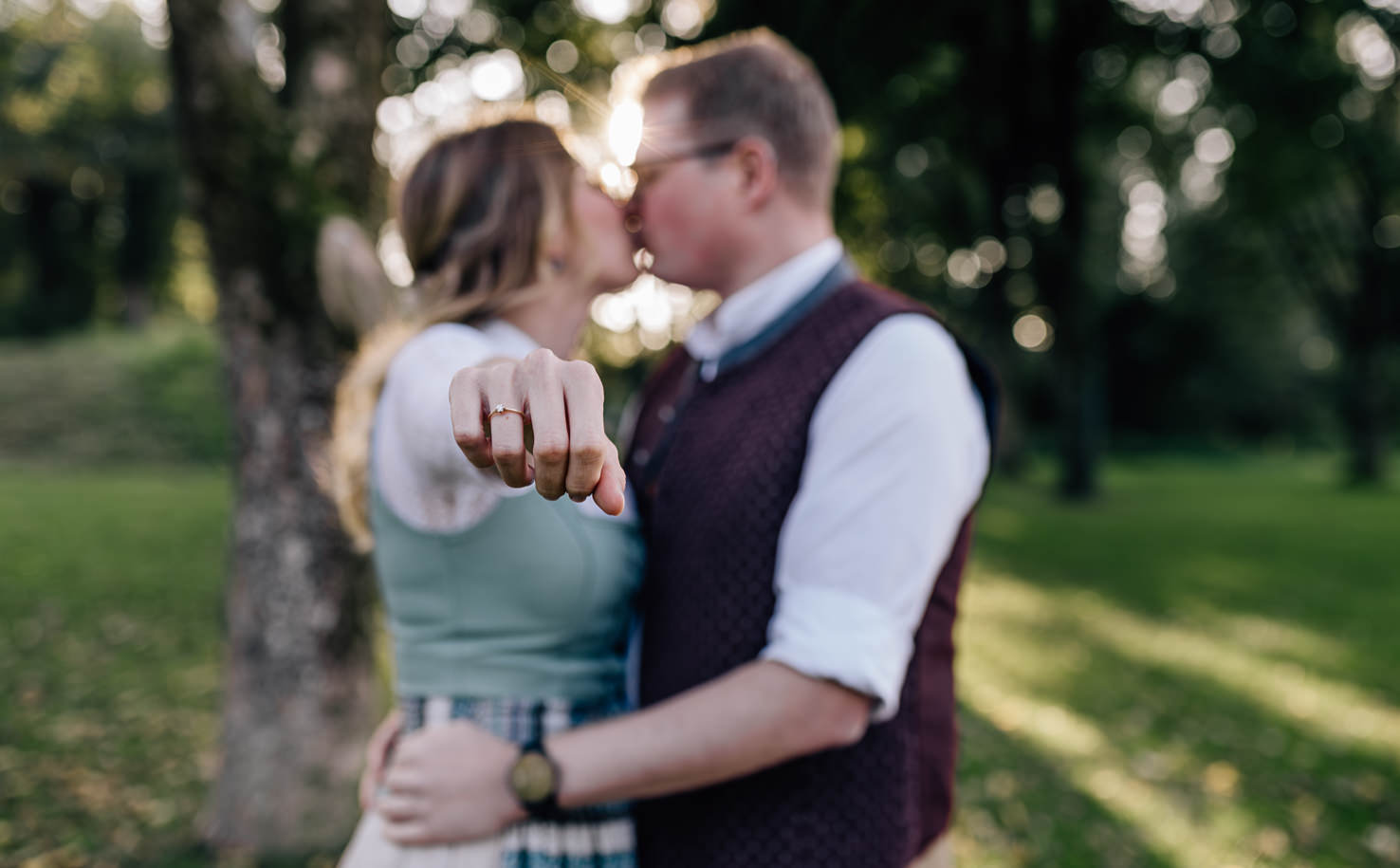 Das romantische Bild von Mica Zeitz zeigt ein verliebtes Paar, das sich in einem malerischen Park küsst, während der Fokus auf dem funkelnden Verlobungsring der Frau liegt. Diese Darstellung von Liebe und Zuneigung unterstreicht die Bedeutung unvergesslicher Momente in der Hochzeitsfotografie.