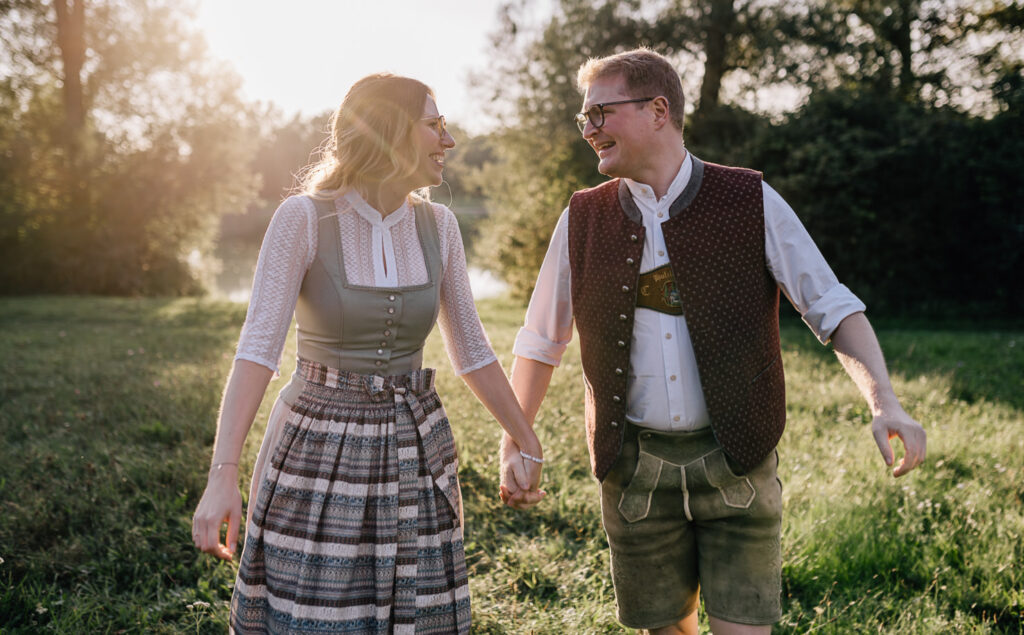 Dieses romantische Bild von einem Paar, das glücklich im bayerischen Aufzug hält, fängt den Charme von Trachtenmode im Freien ein und strahlt eine herzliche Verbindung aus. Fotografiert von Mica Zeitz, vermittelt das Bild ein Gefühl von Liebe und Geborgenheit in einer malerischen Naturkulisse.