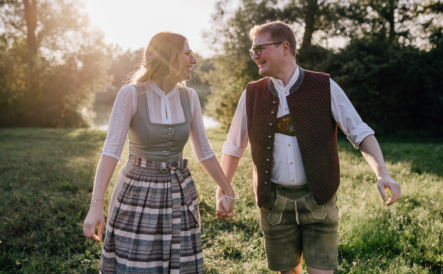 Dieses romantische Bild von einem Paar, das glücklich im bayerischen Aufzug hält, fängt den Charme von Trachtenmode im Freien ein und strahlt eine herzliche Verbindung aus. Fotografiert von Mica Zeitz, vermittelt das Bild ein Gefühl von Liebe und Geborgenheit in einer malerischen Naturkulisse.