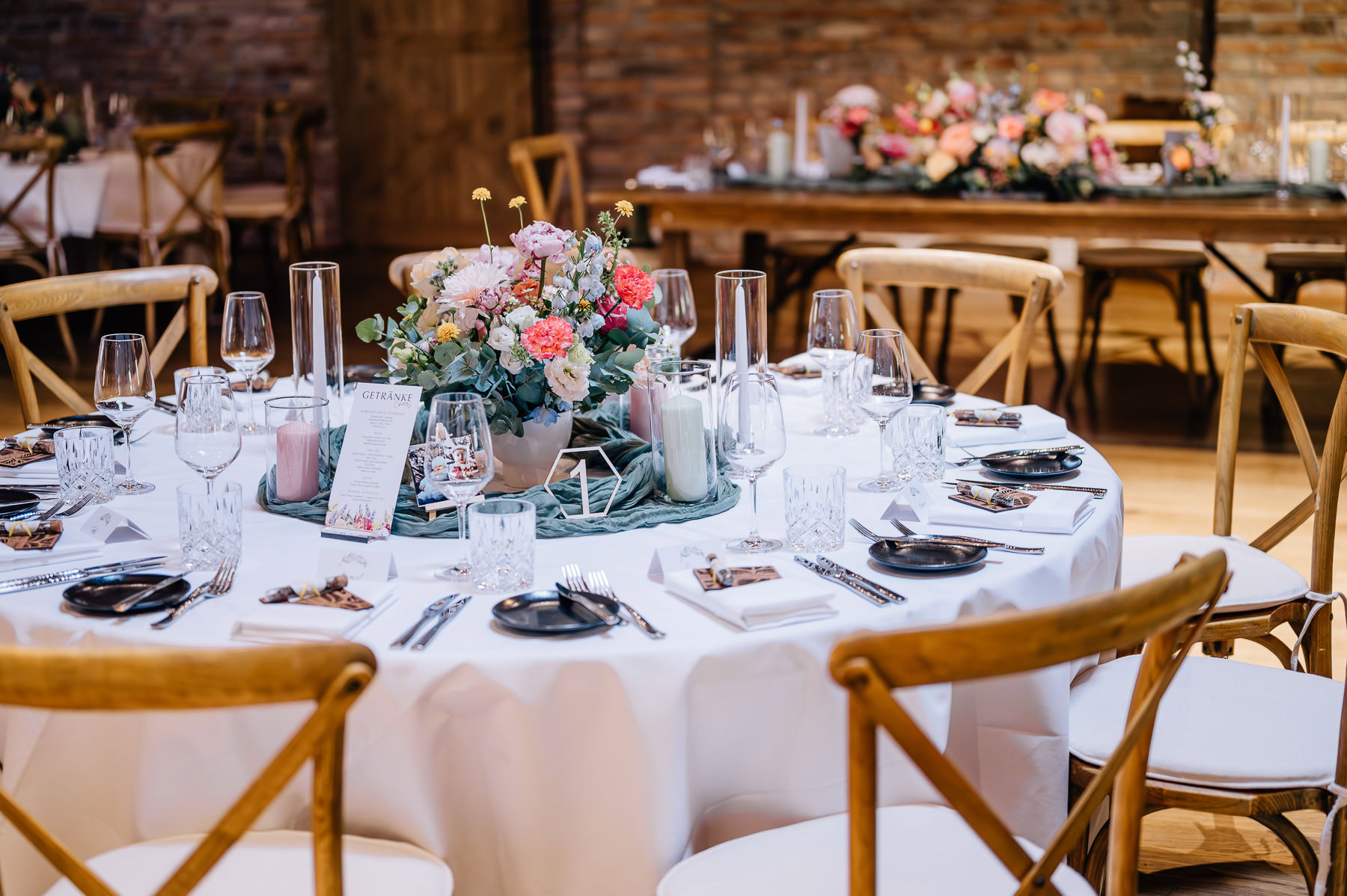 Das Bild zeigt eine elegant eingedeckte Hochzeitstafel in der Eventtenne Pfaffenhofen, dekoriert mit einem Blumenarrangement und stilvollem Geschirr. Diese Hochzeitslocation ist eine hervorragende Empfehlung für unvergessliche Feiern, festgehalten von der Fotografin Mica Zeitz.