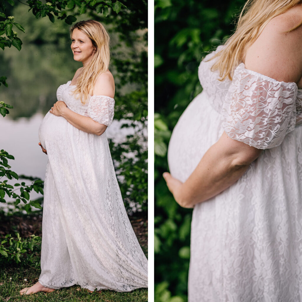 Das Bild zeigt eine schwangere Frau in einem eleganten, weißen Leihoutfit mit Spitzenärmelchen, die vor einer malerischen Kulisse aus Bäumen und Wasser steht. Ihre Hand ruht sanft auf ihrem Babybauch und strahlt eine ruhige Freude aus, die in den Babybauchfotos festgehalten wird, aufgenommen von der Fotografin Mica Zeitz.
