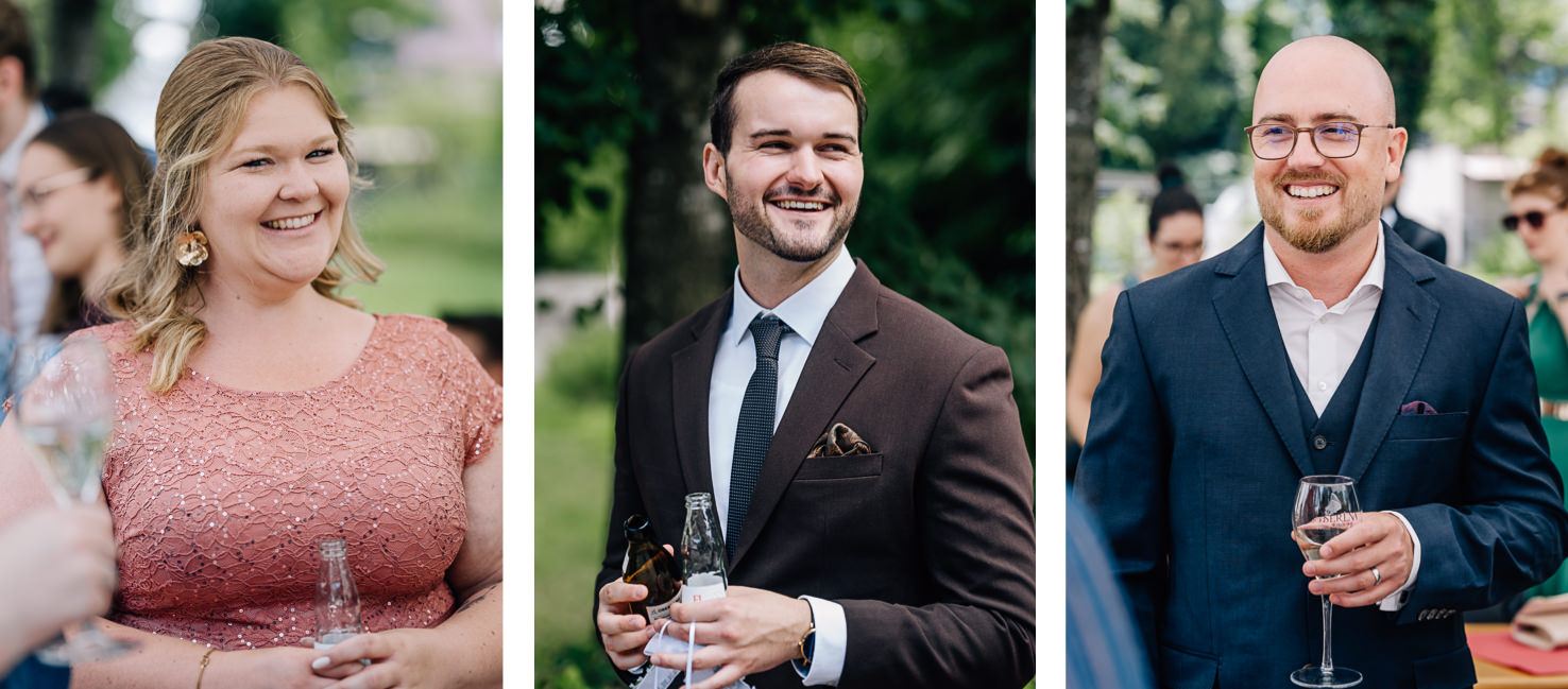 Auf den Hochzeitsfotos aus Olching lächeln freundliche Gäste in eleganter Kleidung, während sie Getränke in der Hand halten. Die fröhliche Atmosphäre und die schöne Naturkulisse unterstreichen die festliche Stimmung, eingefangen von der Fotografin Mica Zeitz.